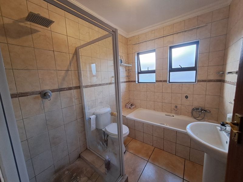 A functional bathroom featuring a separate shower enclosure, built-in bathtub, pedestal sink, and tiled finishes throughout.