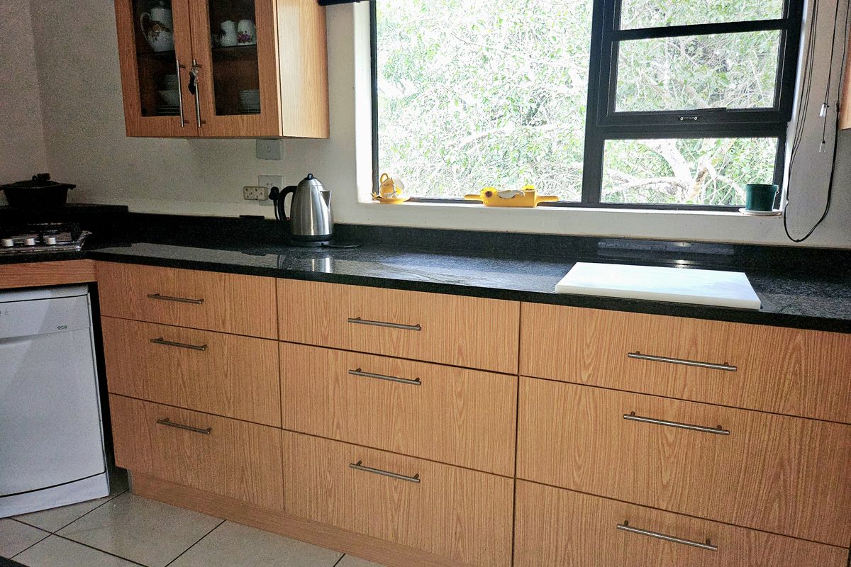 A functional kitchen featuring light wood-look laminate cabinetry, dark granite countertops, and tiled flooring, illuminated by a large window.