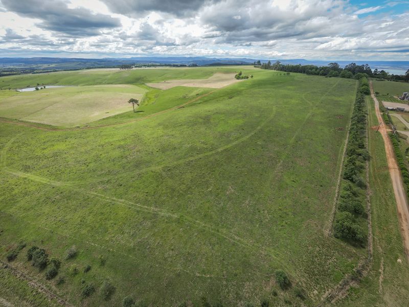 An aerial view of a large, expansive residential vacant land plot featuring rolling green pastures, perimeter fencing, and access to a dirt road.