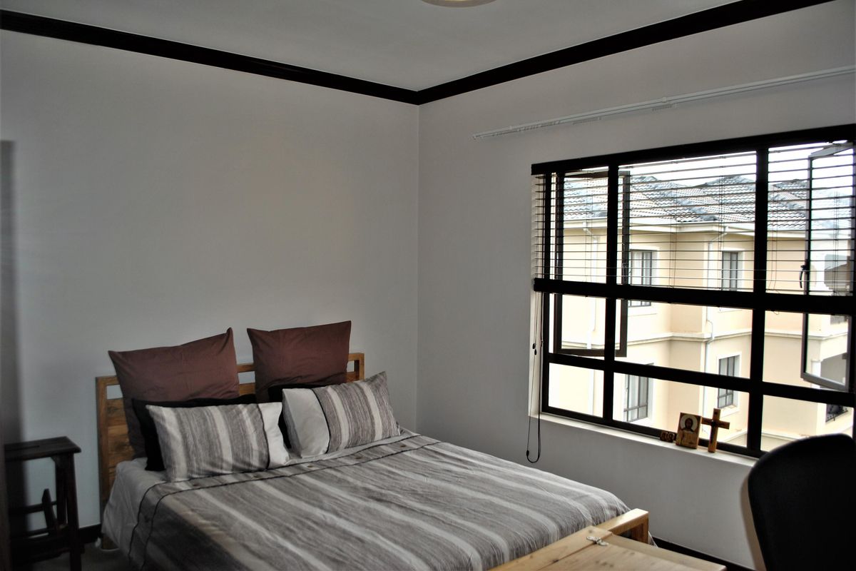 A bedroom featuring dark-framed windows with blinds and contrasting dark crown molding, providing a neutral space with natural light.