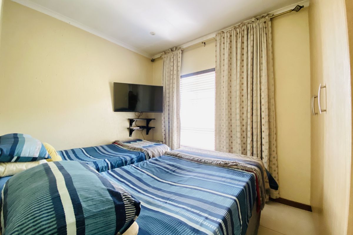 A functional bedroom featuring built-in wardrobe storage, recessed ceiling lighting, and a window dressed with curtains.