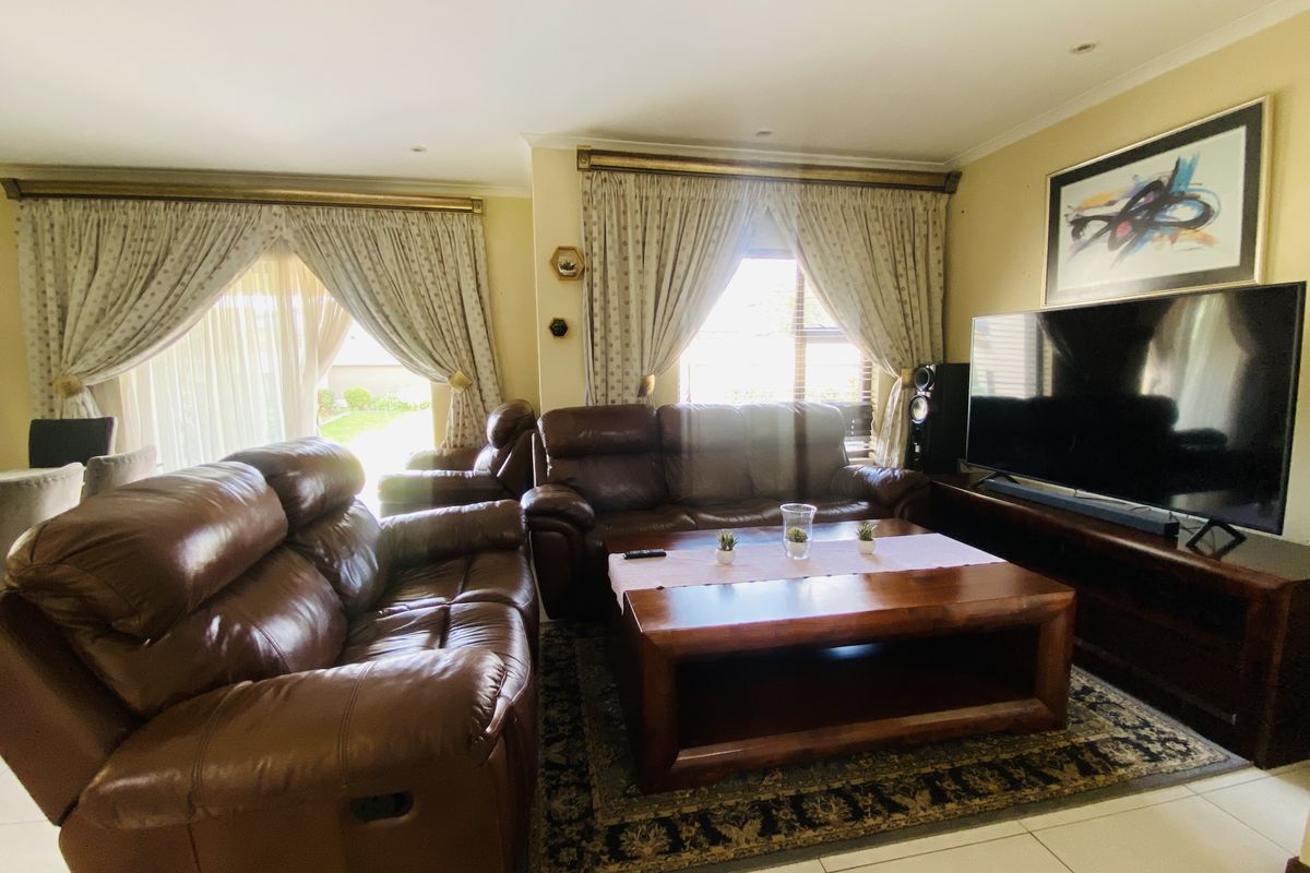 A comfortable living room featuring tiled flooring, recessed downlighting, and large windows with curtain treatments, providing a functional and well-lit space.