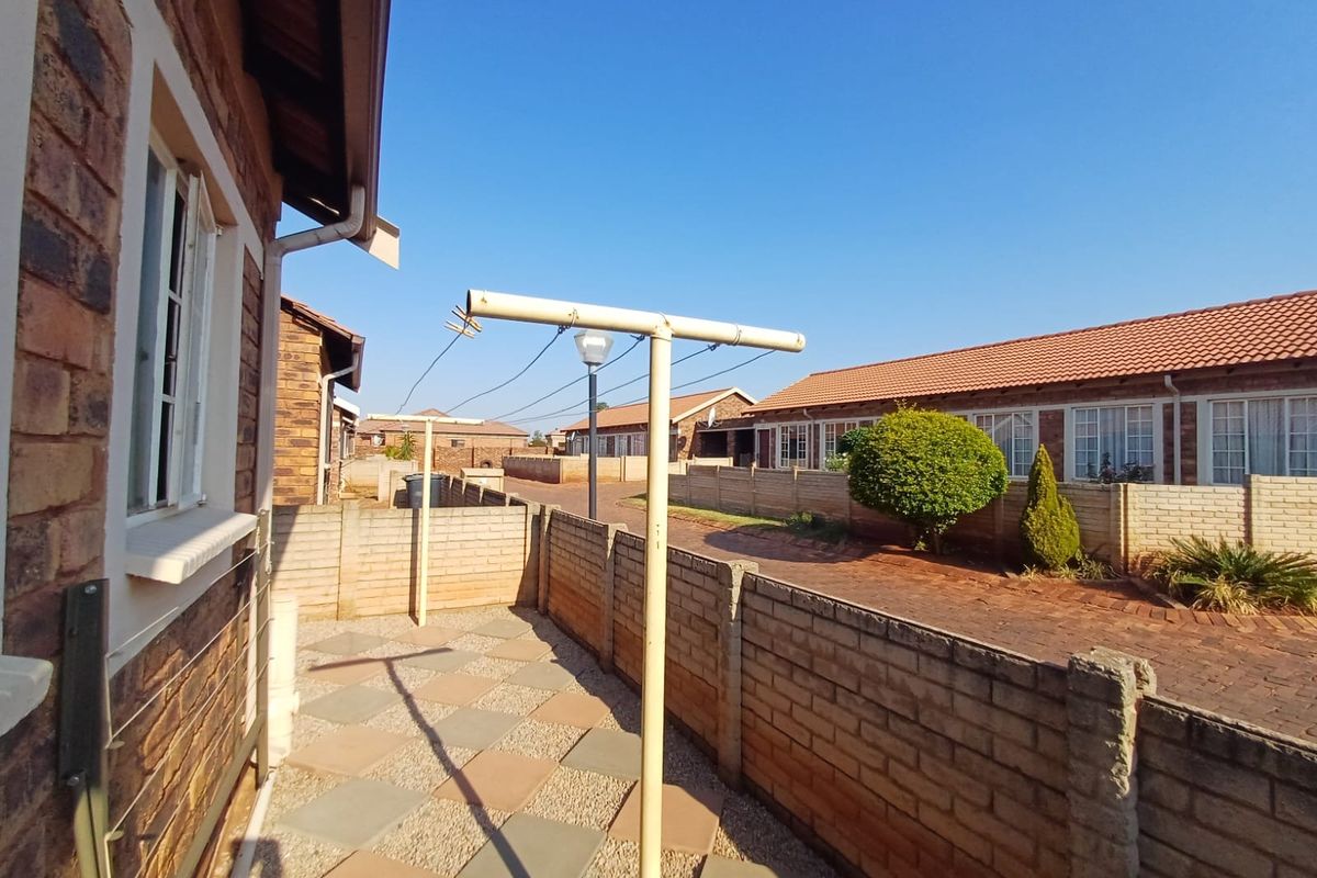 A rear exterior view of the townhouse featuring a paved patio area, brick boundary walls, and a metal washing line.