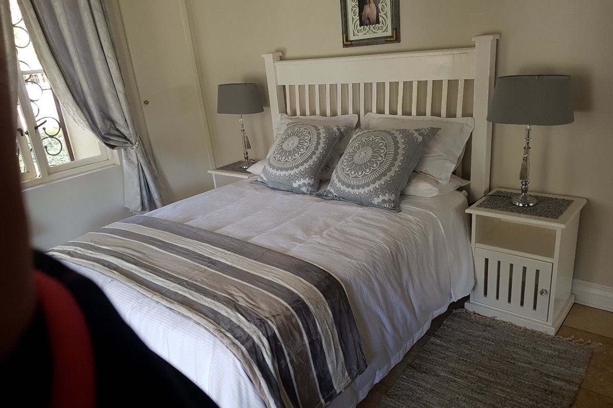 A well-maintained bedroom featuring tiled flooring, a built-in cupboard, and a window fitted with a security gate.