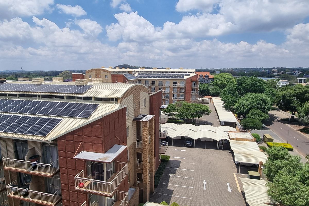 Aerial view of the apartment complex featuring extensive rooftop solar panel installations, covered parking bays, and private balconies.