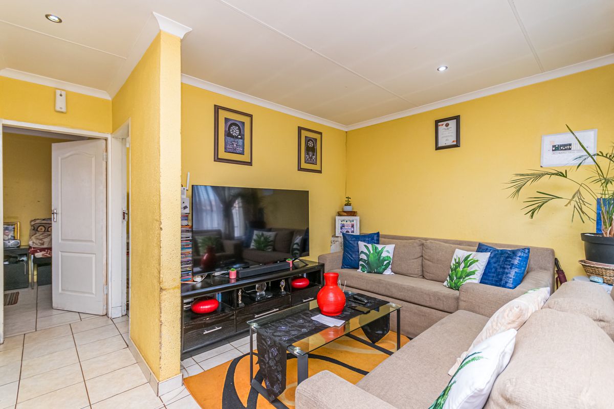 A living room featuring tiled flooring, recessed downlighting, and coved ceilings, providing a functional space with potential for cosmetic updates.