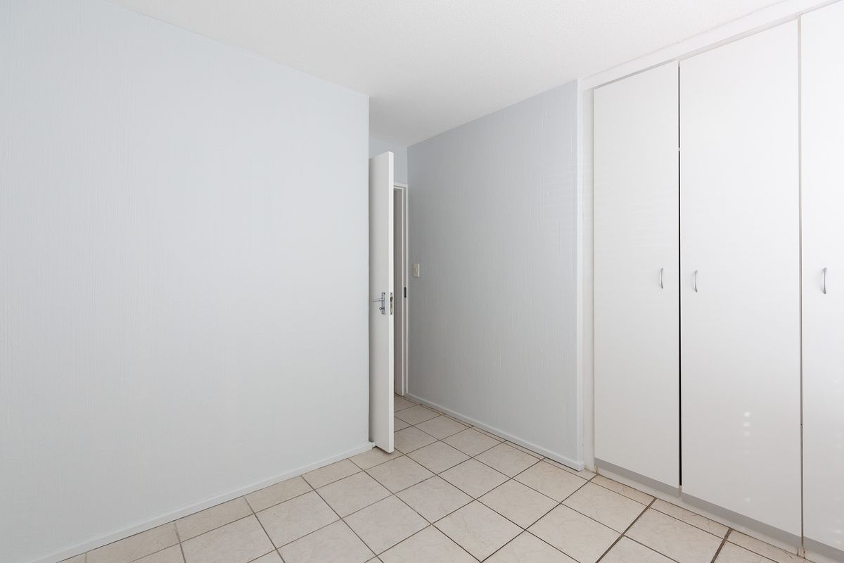 An empty bedroom featuring neutral tiled flooring and built-in white cupboards, offering a clean and versatile space ready for personalization.
