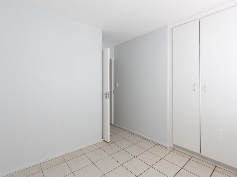 An empty bedroom featuring neutral tiled flooring and built-in white cupboards, offering a clean and versatile space ready for personalization.