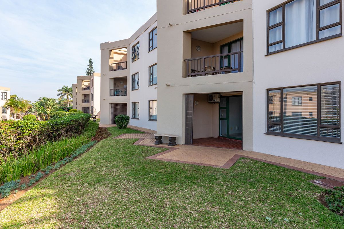 Rear view of the apartment complex featuring ground floor paved patios, landscaped garden areas, and upper-level balconies with aluminium window frames.