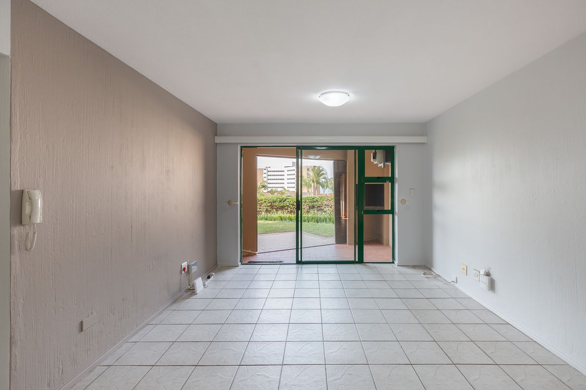 An empty, tiled living room featuring a sliding glass door that opens to an outdoor patio area.