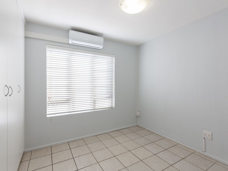 A clean, empty bedroom featuring tiled flooring, built-in cupboards, and a wall-mounted air conditioning unit.