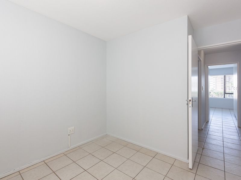 An empty bedroom featuring neutral tiled flooring and white walls, with a doorway leading to a connecting hallway.
