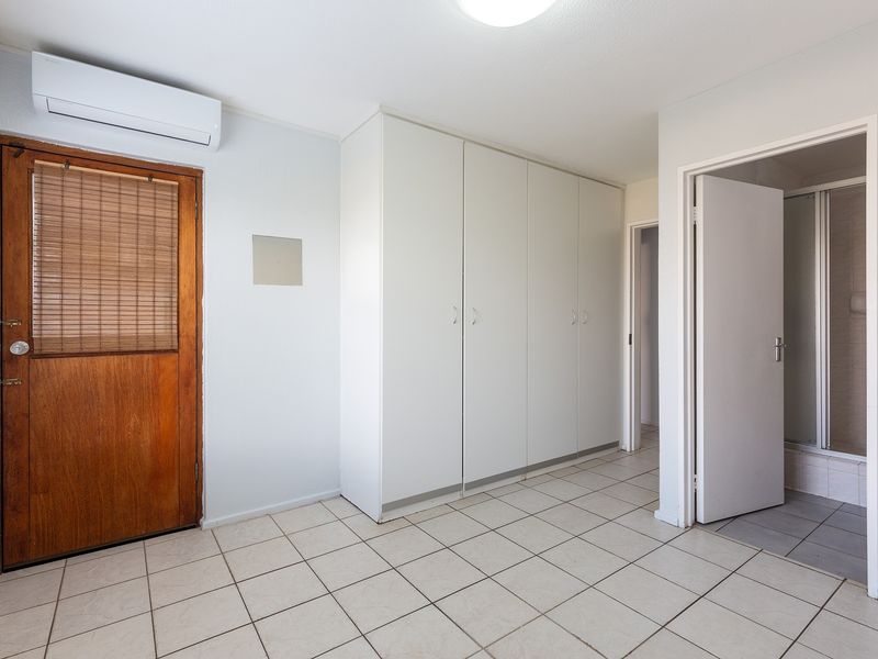 A bright, empty bedroom featuring tiled flooring, built-in cupboards, a split-system air conditioner, and direct access to an en-suite bathroom.