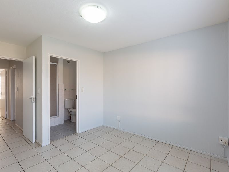 An empty bedroom featuring tiled flooring, neutral walls, and direct access to an en-suite bathroom with a shower.