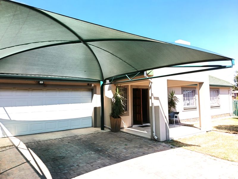 Front exterior view of the house featuring a paved driveway, a large shadeport, and a covered entrance with security bars on the windows.