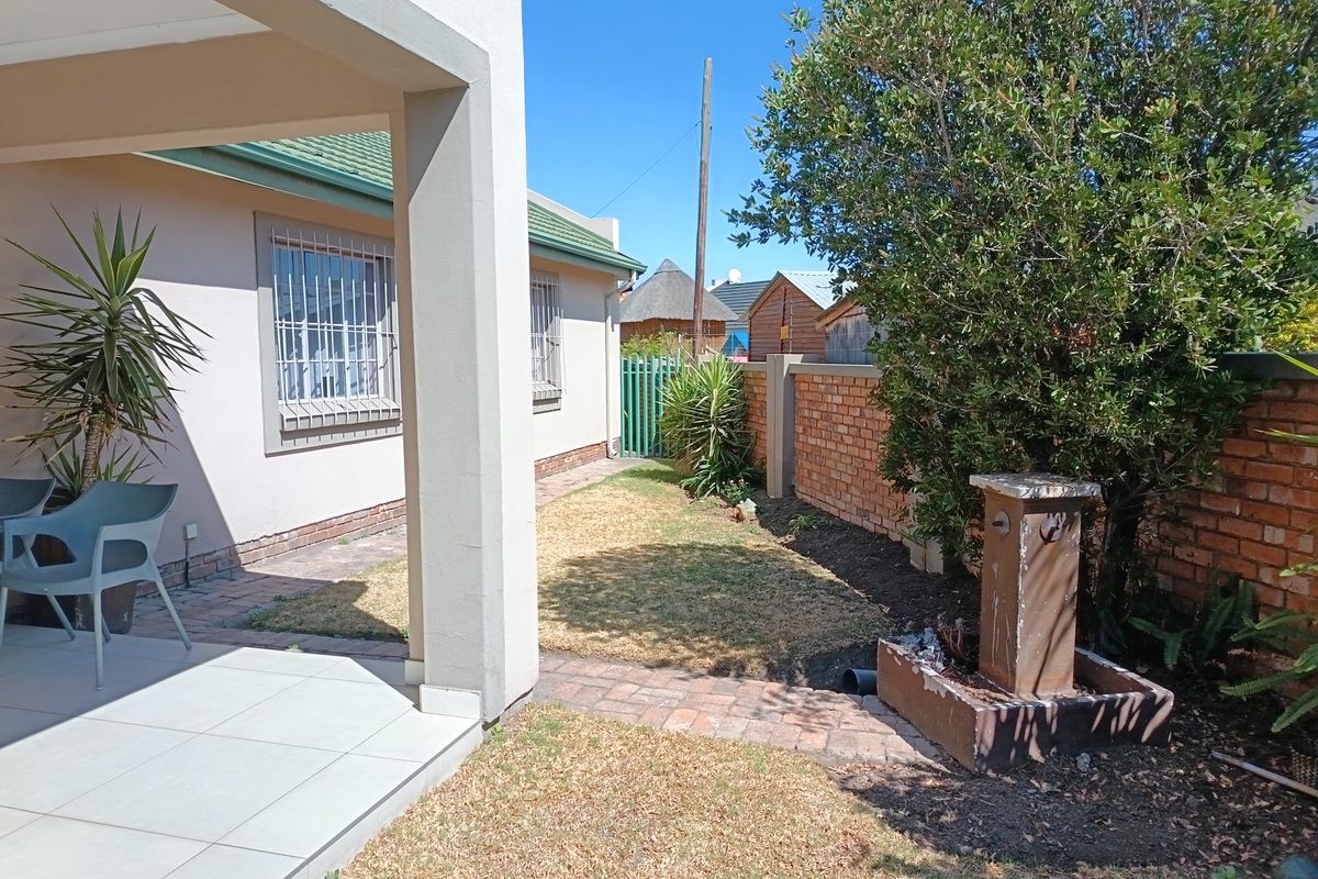 A rear garden area featuring a tiled patio, paved walkway, brick boundary wall, and a small water feature.