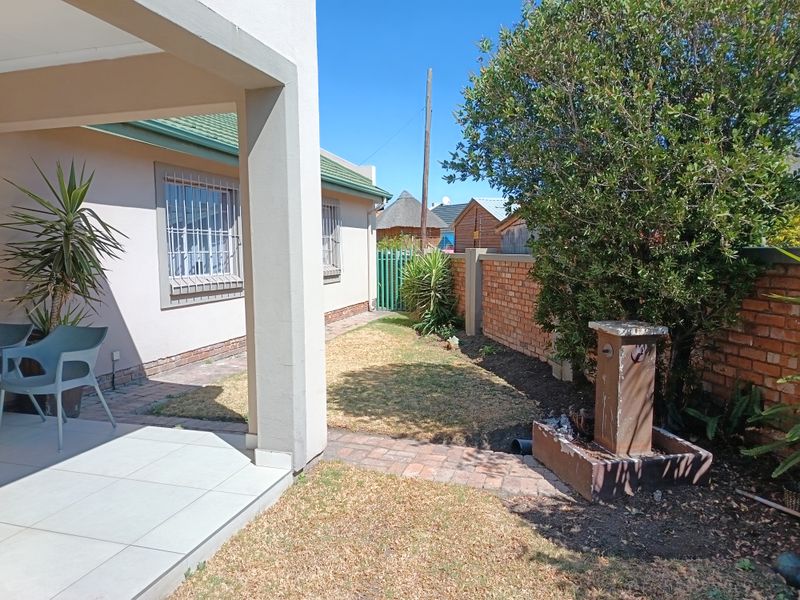 A rear garden area featuring a tiled patio, paved walkway, brick boundary wall, and a small water feature.