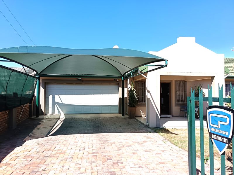 Front elevation of the house featuring a paved driveway, a shade sail carport, a sectional garage door, and secure perimeter fencing.