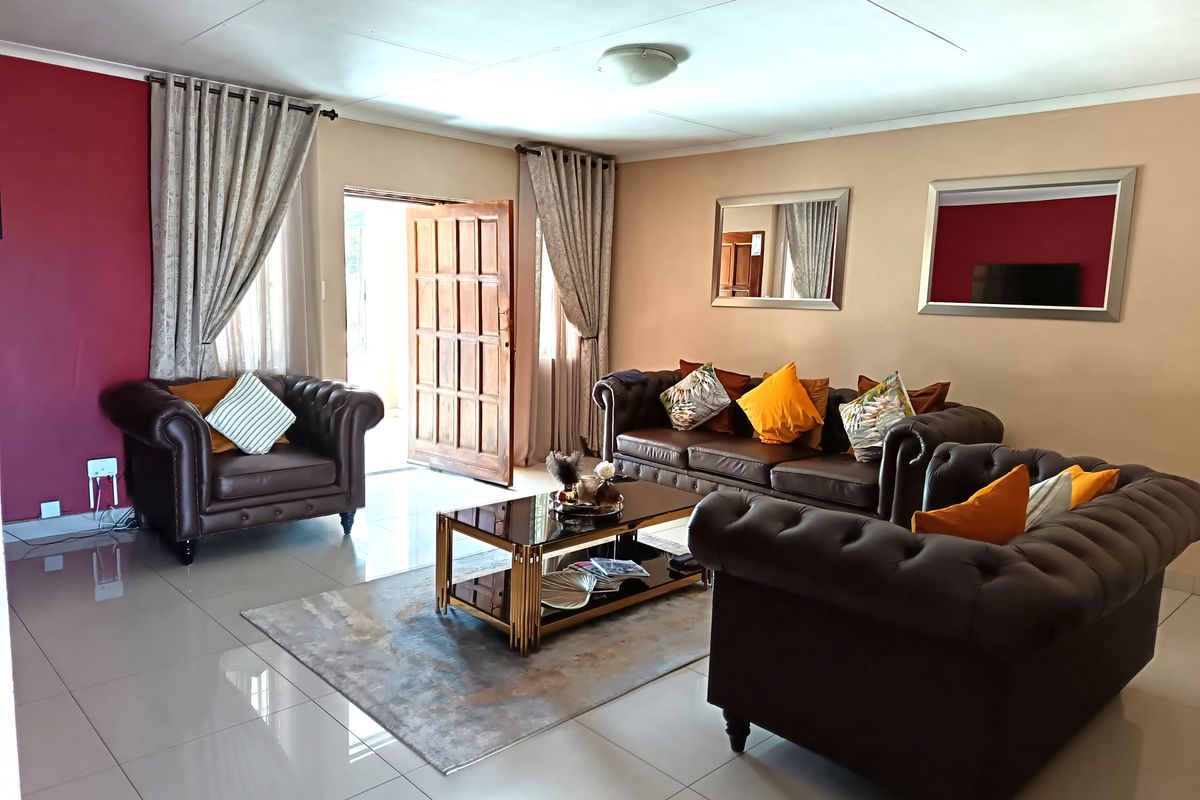 A spacious living room featuring polished tiled flooring, a feature wall, and direct access to the exterior through a timber door.