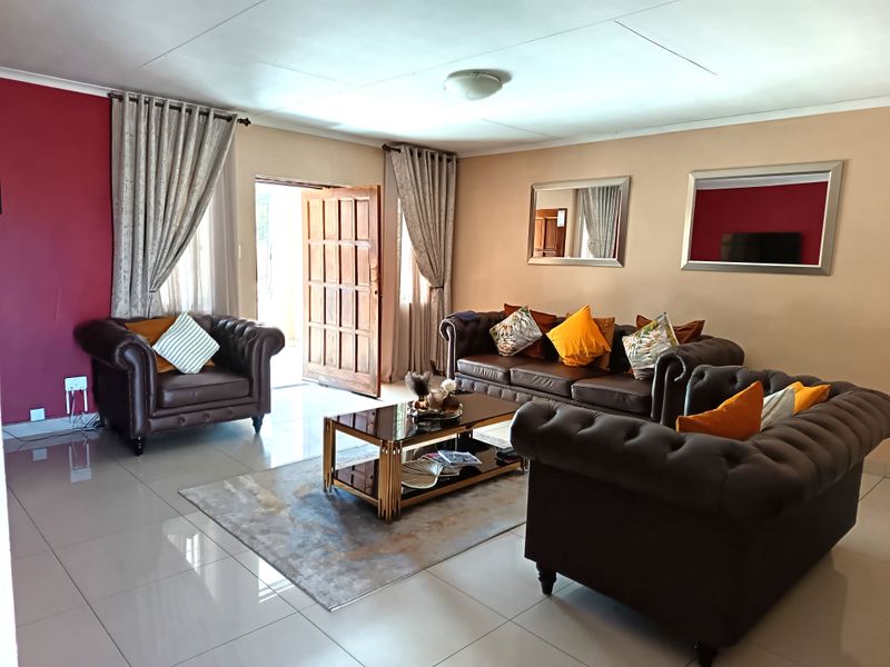 A spacious living room featuring polished tiled flooring, a feature wall, and direct access to the exterior through a timber door.