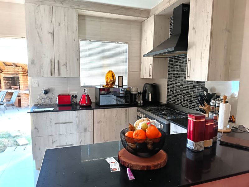 Modern kitchen featuring light wood-grain cabinetry, black granite countertops, a gas hob with extractor fan, and a stylish tiled backsplash.
