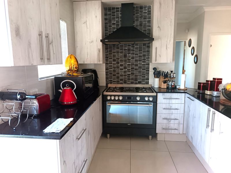 Modern kitchen featuring light wood-grain cabinetry, black granite countertops, a gas hob with extractor fan, and a tiled splashback.
