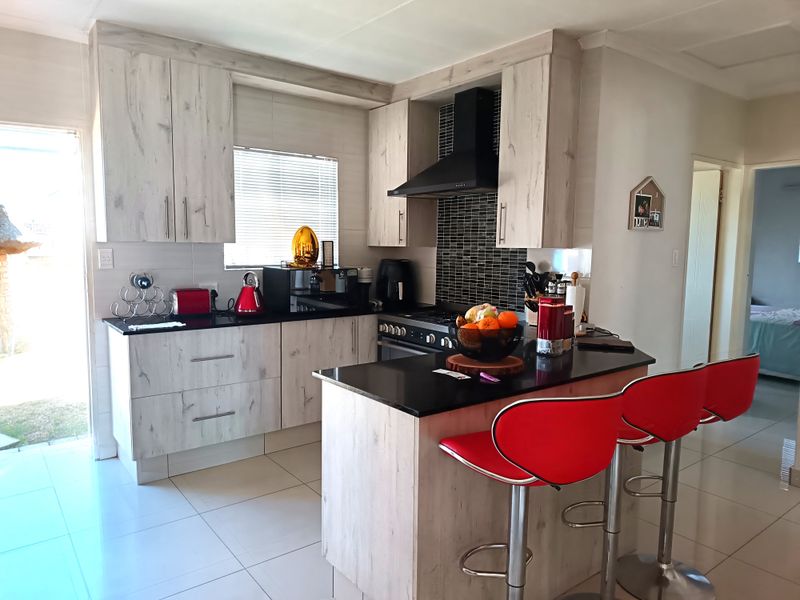 Modern kitchen featuring light wood-grain cabinetry, black granite countertops, a gas hob with extractor fan, and tiled flooring.