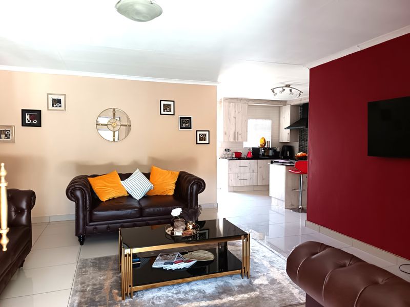 An open-plan living area featuring tiled floors, a modern kitchen with built-in cabinetry, and a distinct red accent wall.