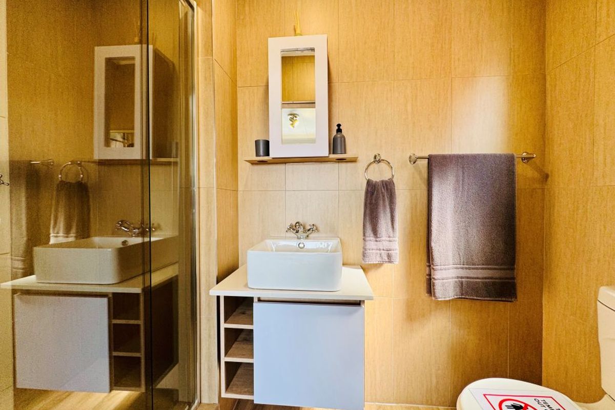 Modern bathroom featuring a glass shower enclosure, wall-mounted vanity with vessel sink, and neutral wall tiling.