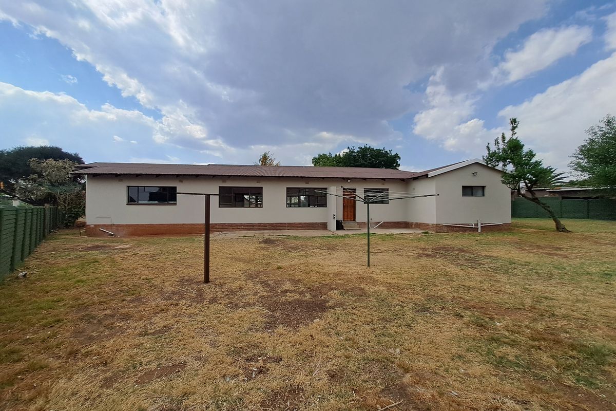 Rear view of the house featuring a concrete patio, corrugated metal roof, and a large backyard with perimeter fencing.