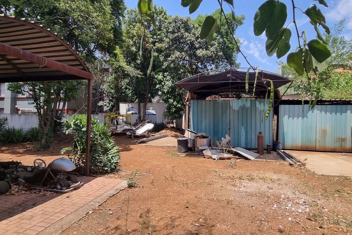 Rear outdoor area featuring a metal carport structure and a corrugated metal shed, set within a large, unlandscaped yard with perimeter walling.