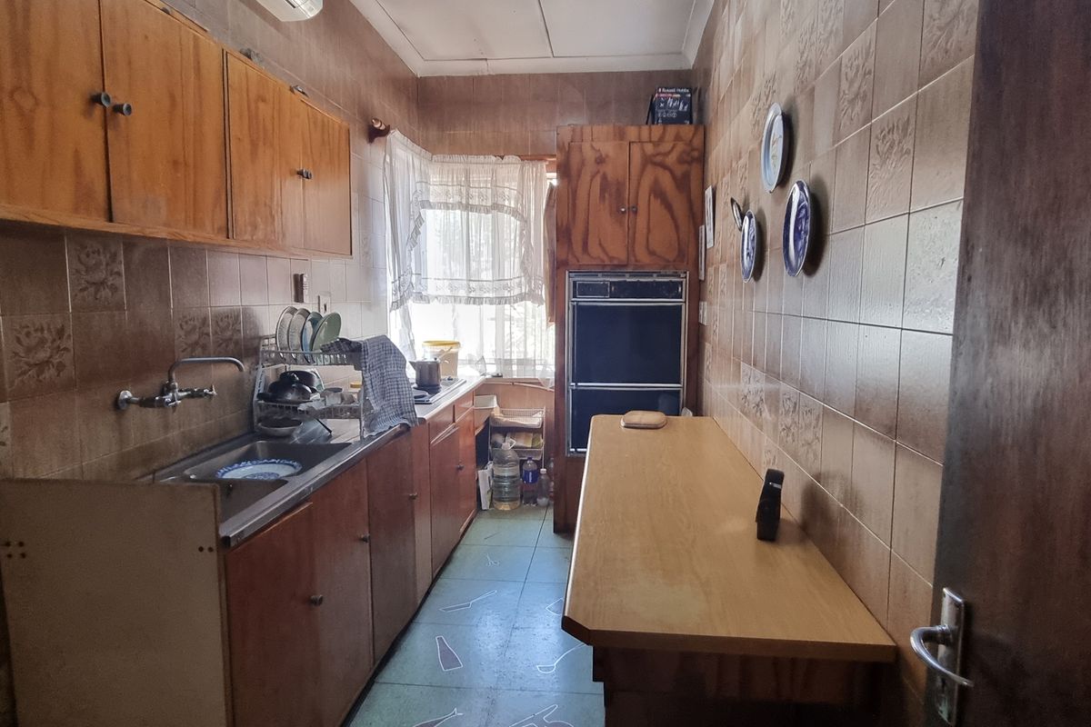 A dated kitchen featuring original wooden cabinetry, a built-in double wall oven, tiled walls, and a functional layout with a breakfast counter.
