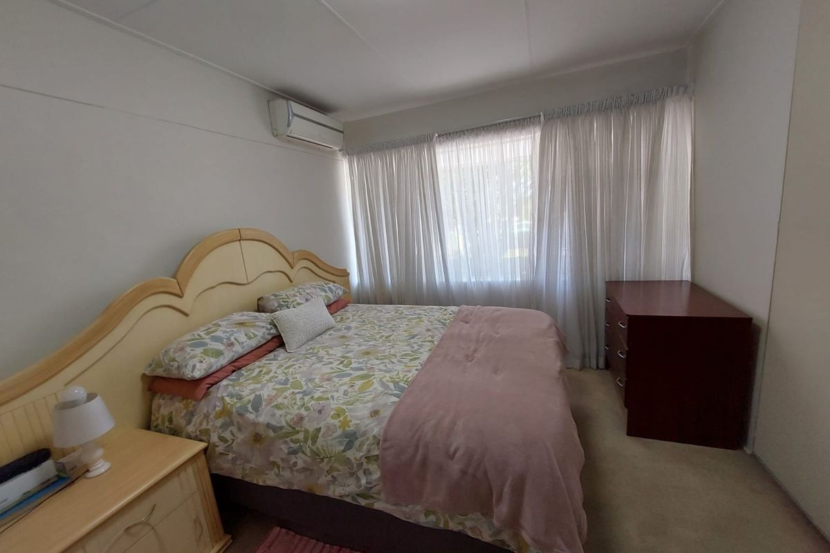 A functional bedroom featuring carpeted flooring, a wall-mounted split-system air conditioner, and built-in wardrobe storage.