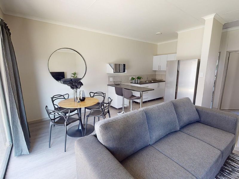 An open-plan living and dining area featuring a compact kitchen with modern cabinetry, a breakfast bar, and sliding doors leading to the exterior.