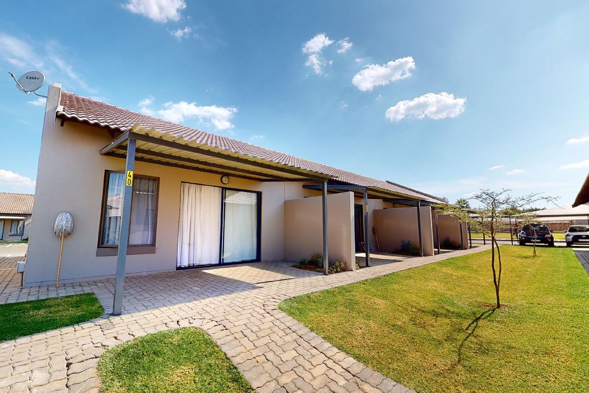 Rear view of a residential unit featuring a paved patio area, covered pergola, and sliding glass doors leading into the home.