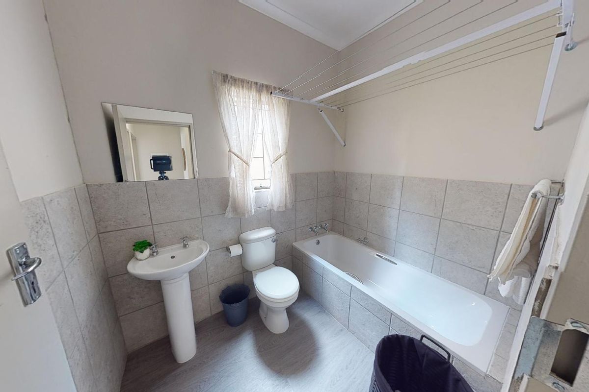 A functional bathroom featuring a pedestal basin, toilet, and bathtub with tiled surrounds, complemented by a wall-mounted drying rack.