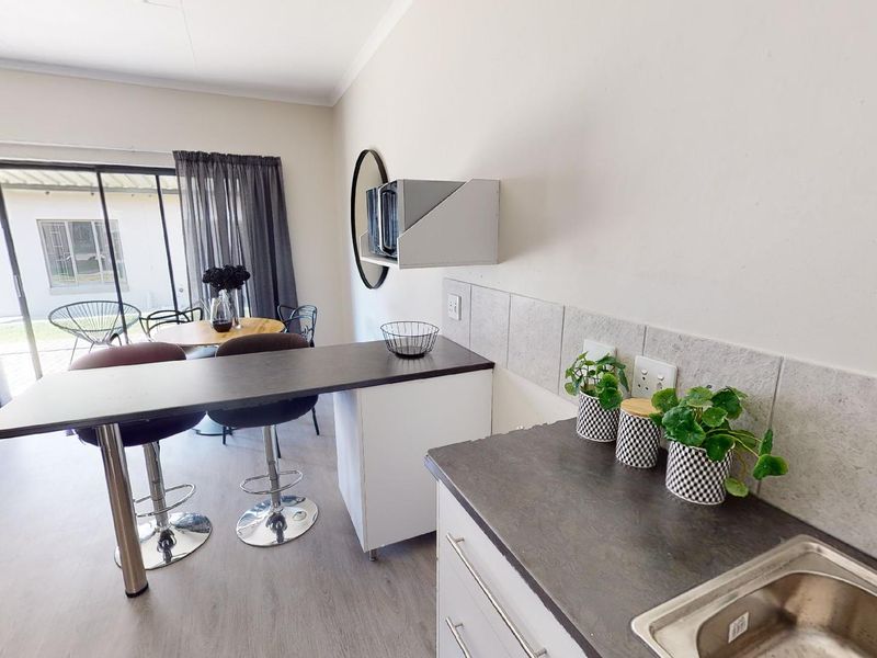 An open-plan living and kitchen area featuring laminate flooring, a built-in breakfast bar, tiled backsplash, and sliding glass doors leading to the exterior.
