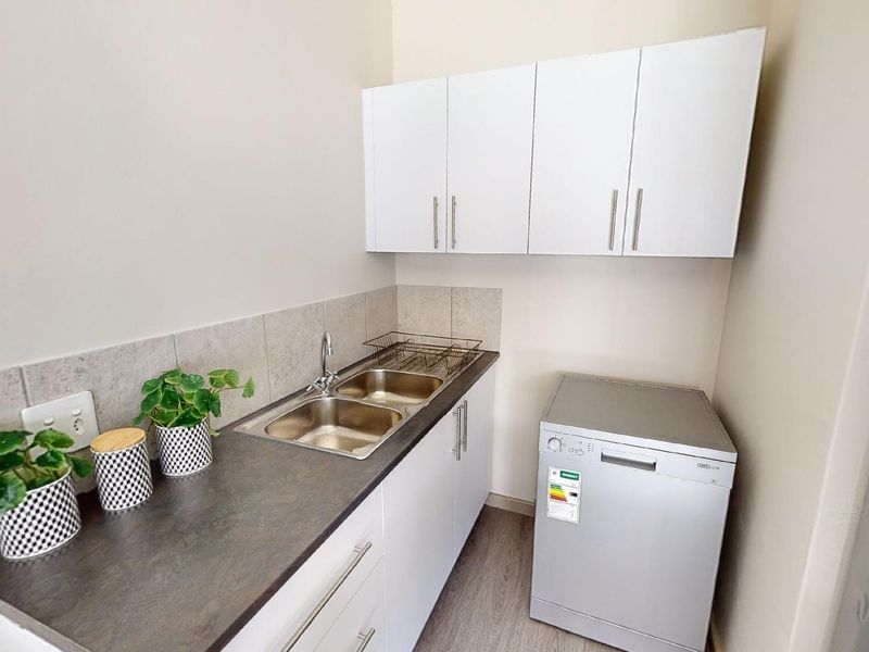 A compact and functional scullery area featuring a double sink, laminate countertops, tiled backsplash, and ample built-in cabinetry for storage.