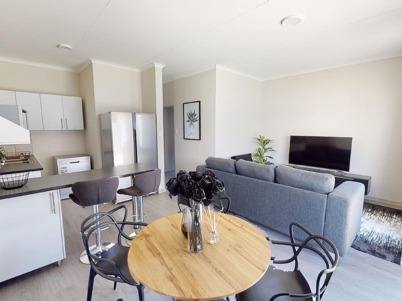 A bright open-plan living and kitchen area featuring modern cabinetry, a breakfast bar, and light-toned laminate flooring throughout the space.