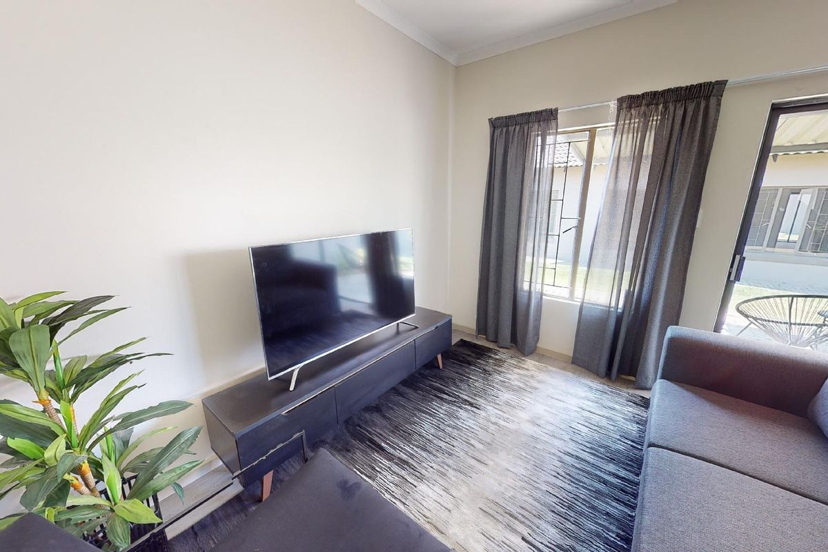 A bright living room featuring a sliding glass door providing access to the exterior and a window with curtains.