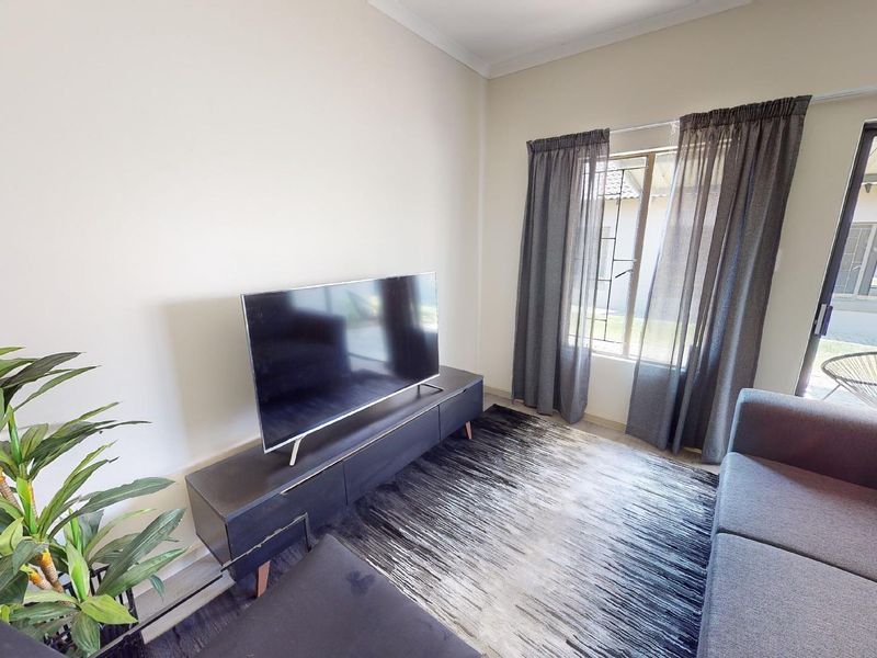 A bright living room featuring a sliding glass door providing access to the exterior and a window with curtains.