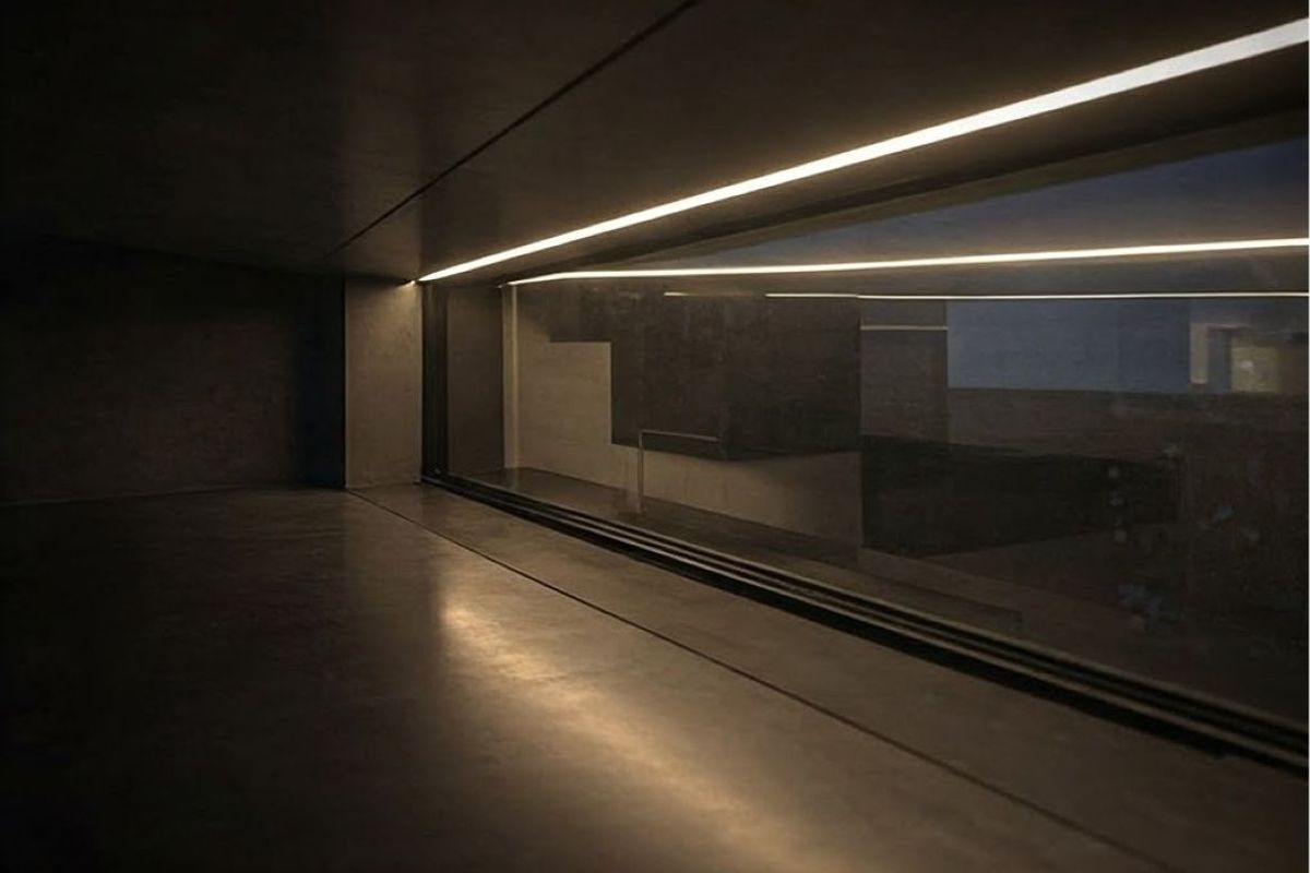 A minimalist, modern living space featuring polished concrete floors, recessed linear lighting, and a large horizontal window providing a sleek, contemporary aesthetic.