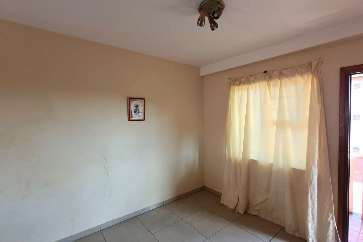 An empty bedroom featuring tiled flooring and a ceiling-mounted light fixture, with walls showing visible scuff marks and signs of wear.