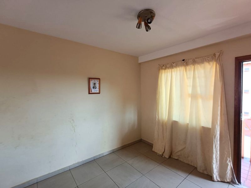 An empty bedroom featuring tiled flooring and a ceiling-mounted light fixture, with walls showing visible scuff marks and signs of wear.