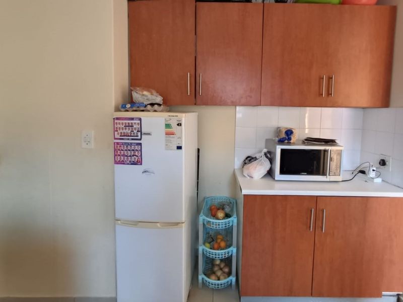 A functional kitchen area featuring wood-look laminate cabinetry, white tiled splashbacks, and a clean countertop workspace.