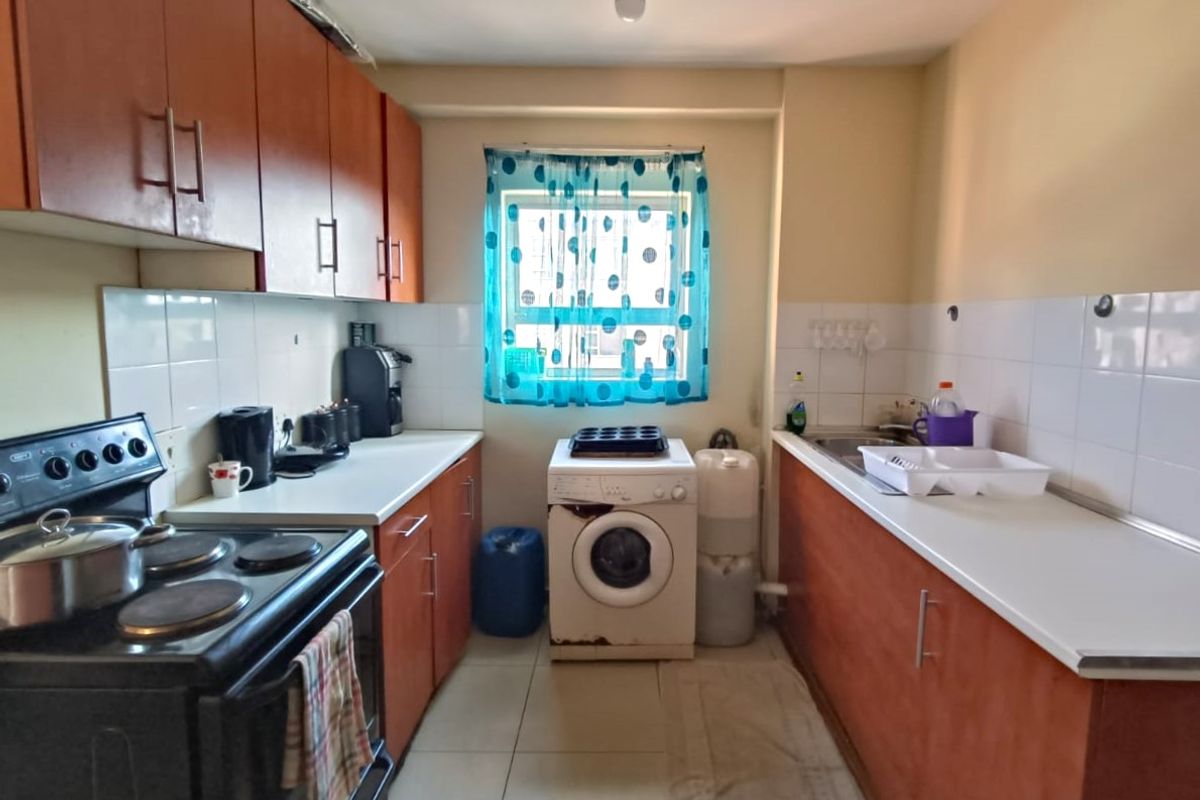 A functional galley-style kitchen featuring laminate cabinetry, tiled backsplash, and tiled flooring, offering a practical layout for daily meal preparation.
