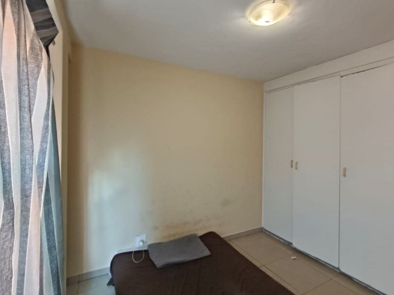 A bedroom featuring built-in cupboards and tiled flooring, requiring some cosmetic attention to the walls.