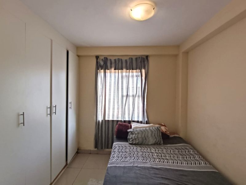 A functional bedroom featuring built-in cupboards, tiled flooring, and a window with natural light.