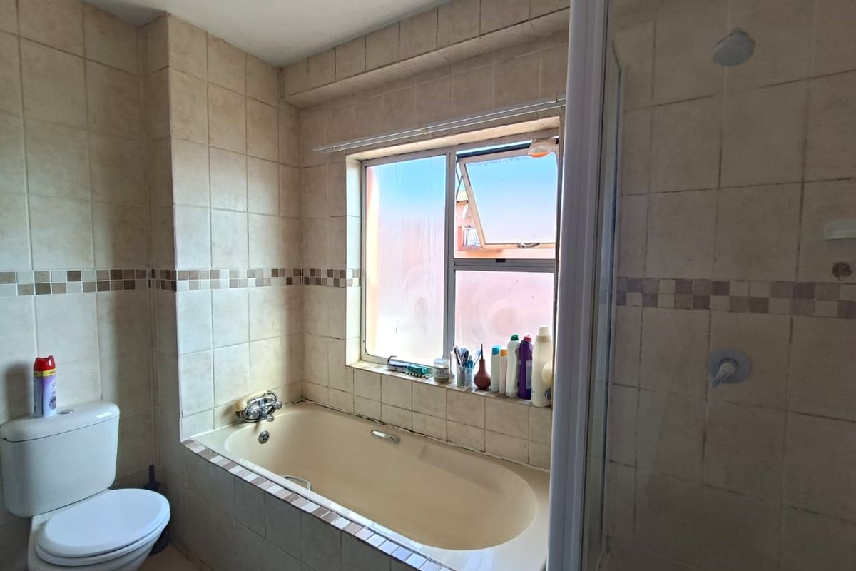 A functional bathroom featuring a built-in bathtub, a separate shower enclosure, and a toilet, finished with neutral ceramic wall tiles.