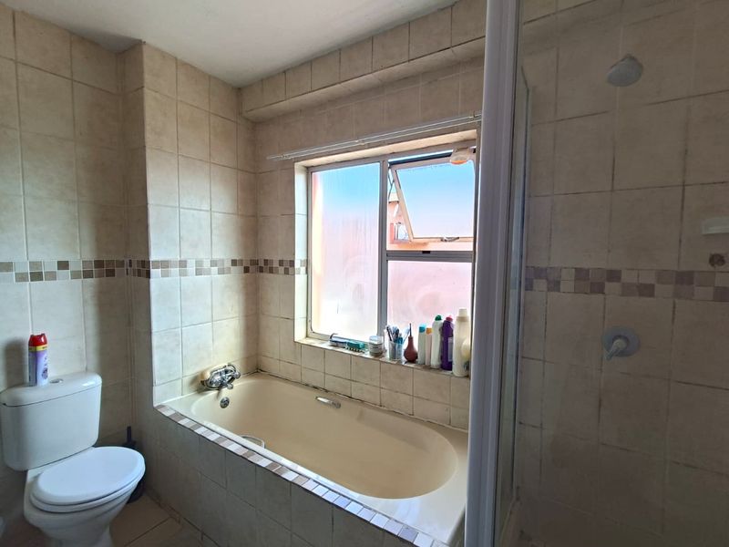 A functional bathroom featuring a built-in bathtub, a separate shower enclosure, and a toilet, finished with neutral ceramic wall tiles.